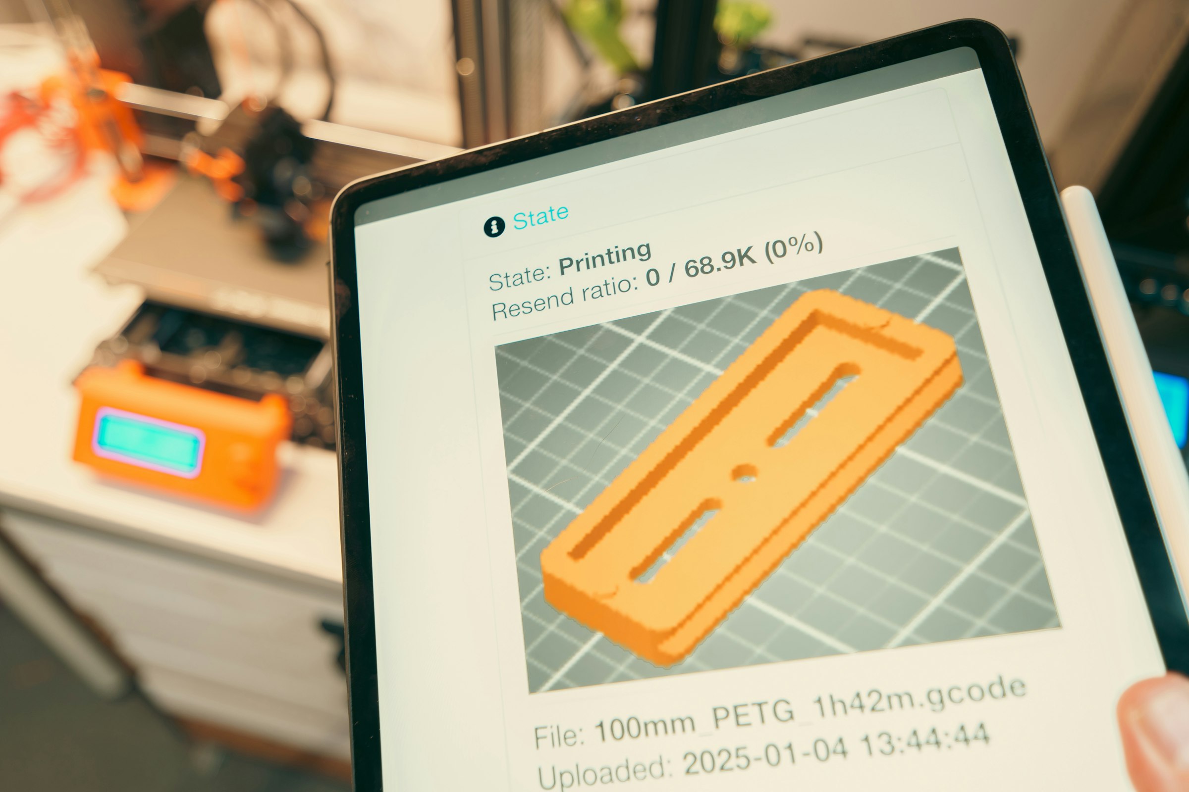 Tablet mostrando el progreso de una impresión 3D en curso con la impresora al fondo
