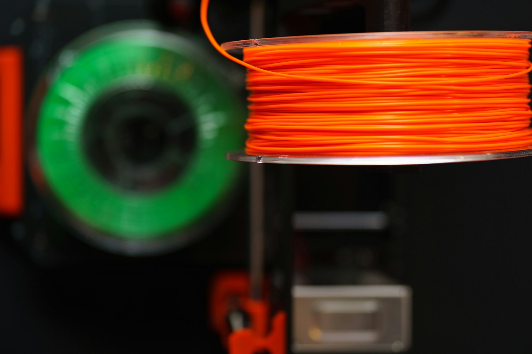 Bobinas de filamento naranja y verde montadas en una impresora 3D