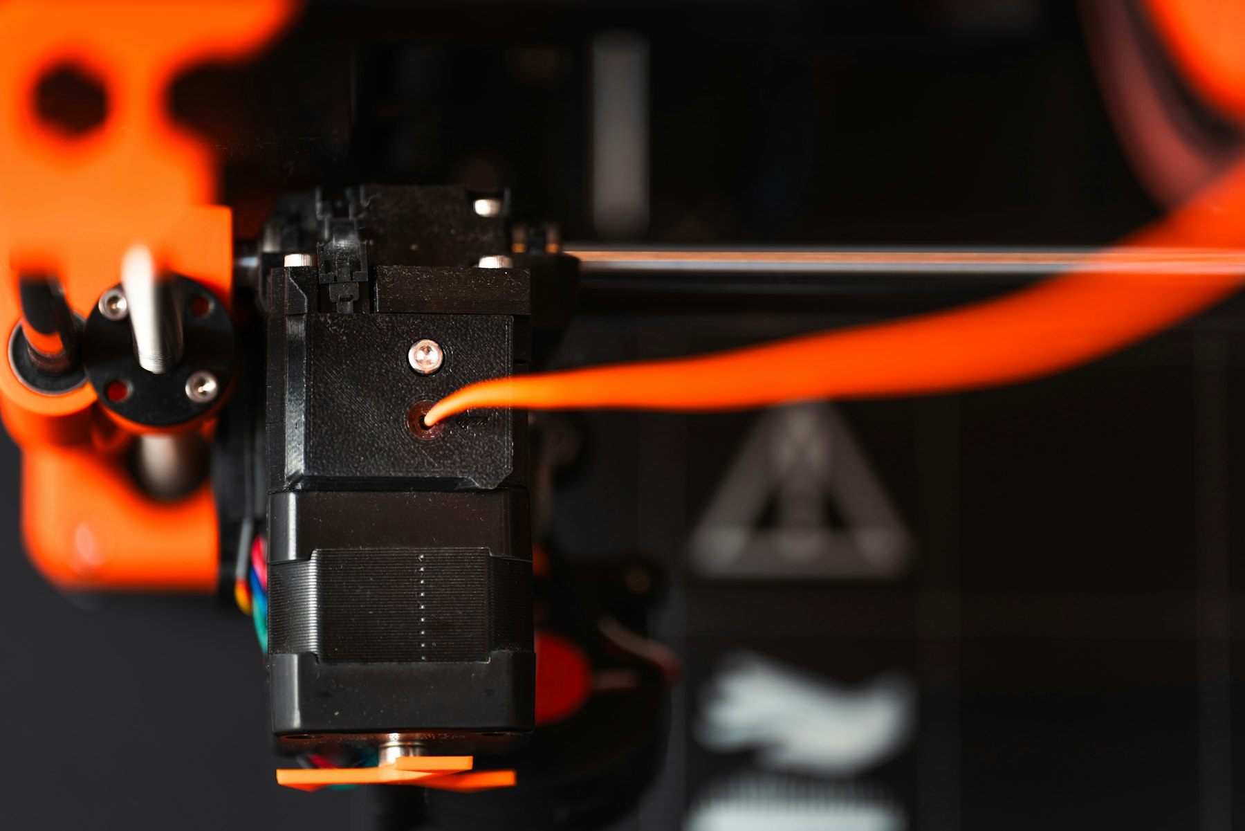 Primer plano del extrusor de una impresora 3D depositando filamento naranja