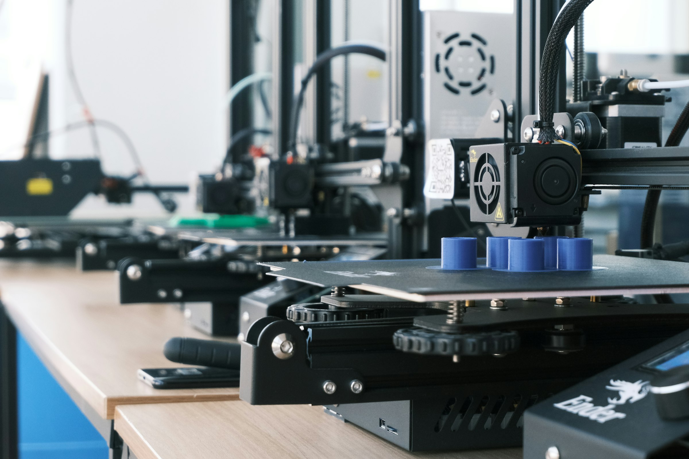 Hilera de impresoras 3D imprimiendo piezas cilíndricas azules en un taller